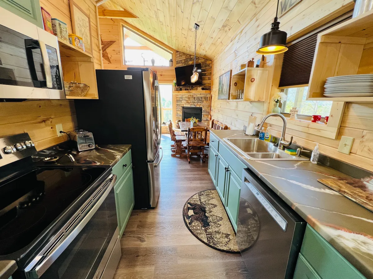 An open kitchen and dining area seamlessly connected to the living space, featuring modern appliances, a wooden dining table, a stone fireplace, and large windows that bring in natural light. The inviting setting is perfect for cooking, dining, and gathering with loved ones.