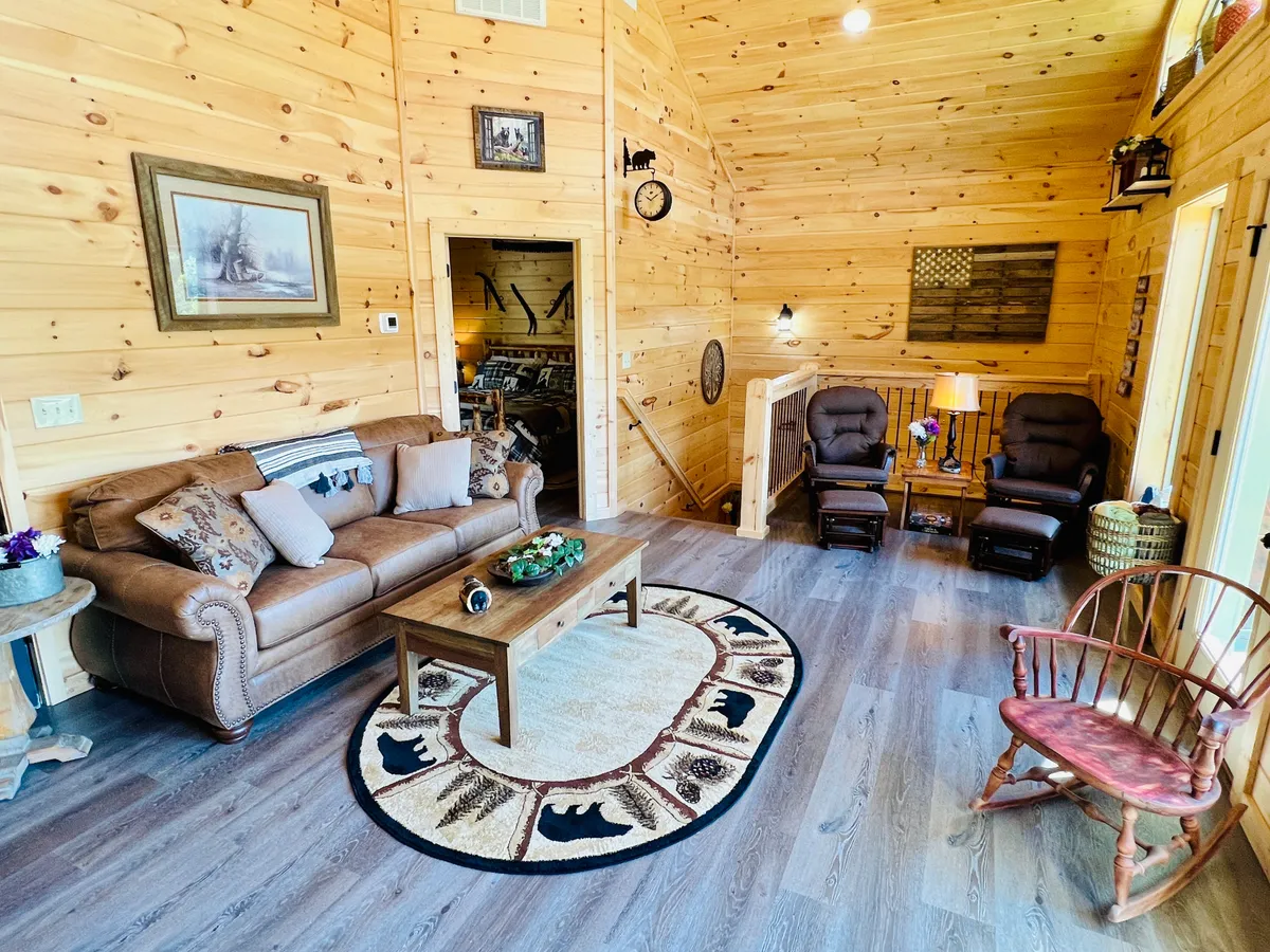 A cozy living area featuring a plush leather couch, wooden coffee table, area rug with animal motifs, and two inviting recliners. The space is warm and inviting, ideal for relaxation, reading, or socializing with friends and family.