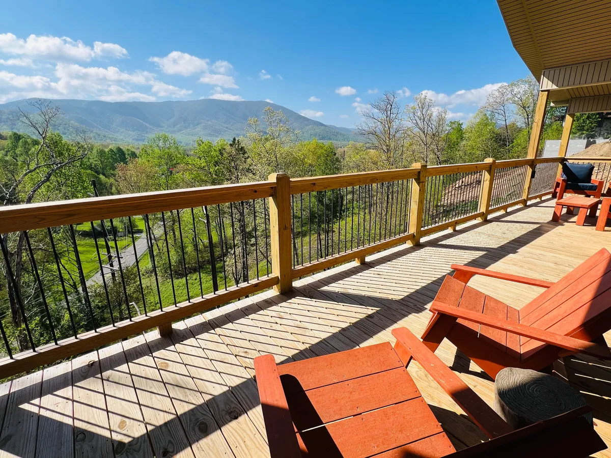 A peaceful exterior shot of a wooden deck framed by lush greenery, with two red Adirondack chairs perfectly positioned to face the mountain view. The setting is intimate and inviting, ideal for couples to share moments at sunrise or under the stars.