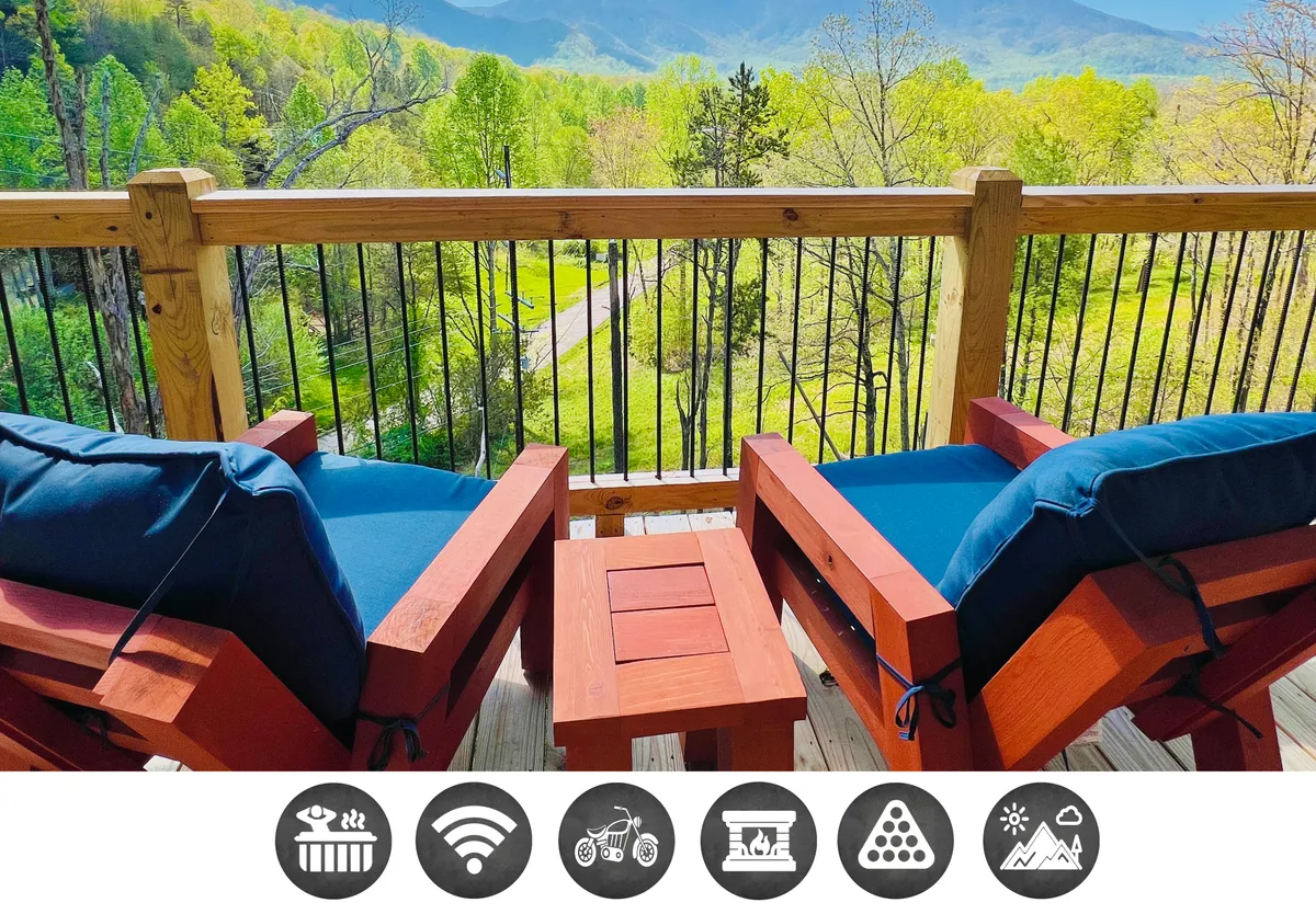 The image features the cabin’s inviting wooden deck furnished with comfortable chairs and a small table, all oriented toward a spectacular mountain view. The serene setting is perfect for relaxing, enjoying nature, socializing, or sipping drinks as the sun sets over the Great Smoky Mountains.