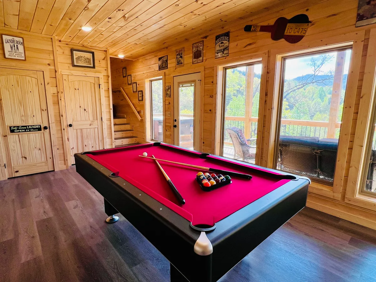 This image features a dedicated game room with a pool table, large windows, wooden walls, and playful decorative signs. The space is bright and inviting—ideal for engaging group activities and memorable game nights with friends or family.